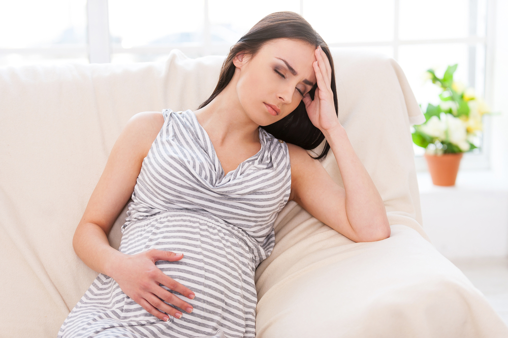 young pregnant woman rests on couch looking exhausted