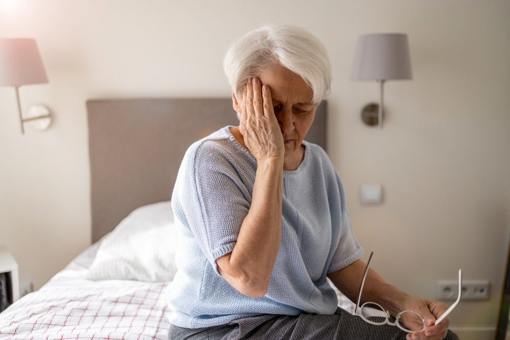 older woman with white hair has headache in bed