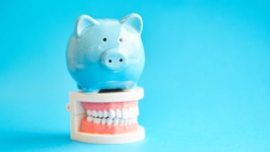 Piggy bank on top of dental model representing cost considerations for dental implants versus traditional dental solutions.