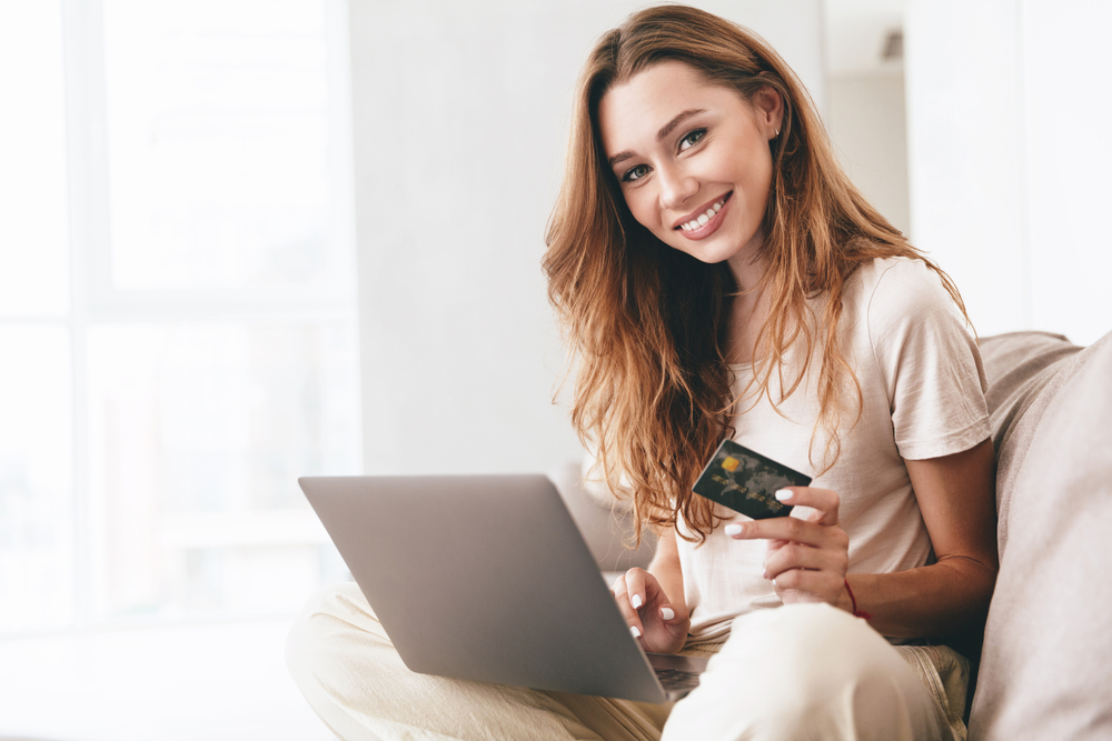 red-headed woman using laptop holds credit card