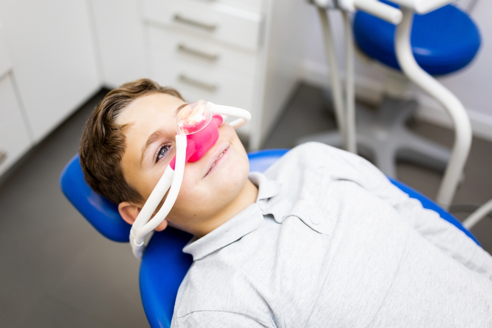 little boy in dental chair wears pink nitrous oxide mask