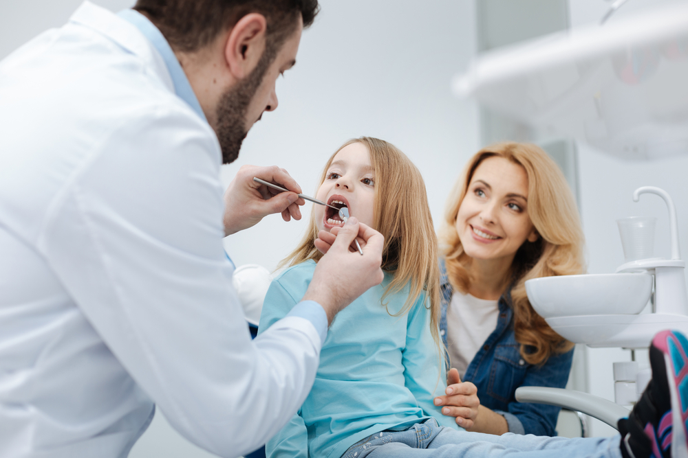 child undergoing dental exam while being held by parent
